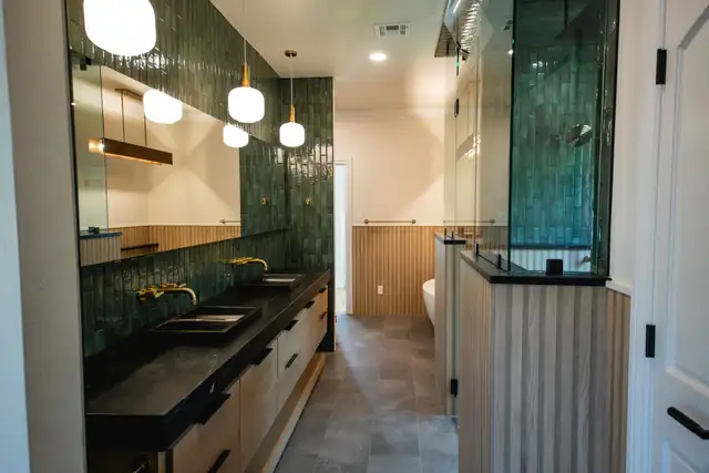 Stone Gate Lodge bathroom with green handmade tile walls, a long dark-topped double vanity and a glass shower enclosure