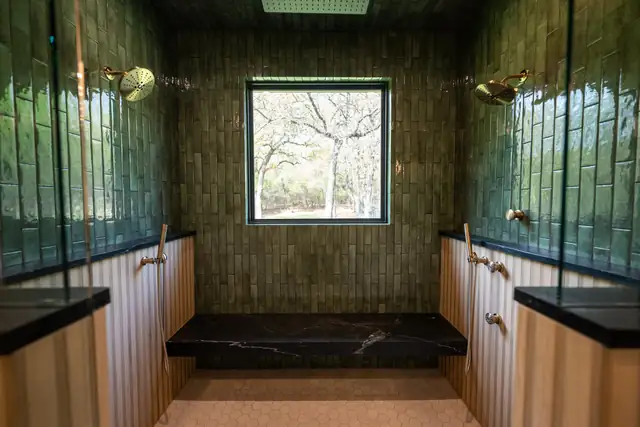 Walk-in shower with green handmade tile walls, dual showerheads and a black stone bench