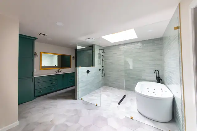 Primary bathroom with green cabinetry, a walk-in glass shower and a white soaking tub under a skylight