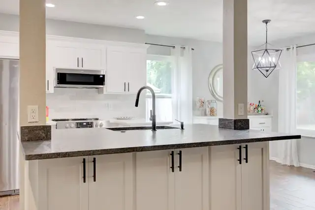 Kitchen with white cabinetry, dark countertops and a central island with a black faucet