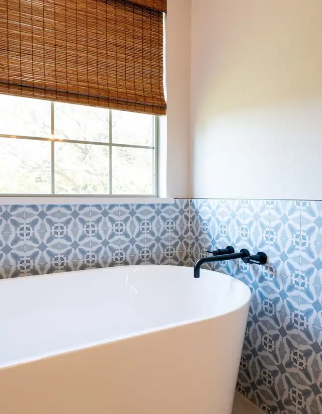 White soaking tub with a matte black wall-mounted faucet and blue patterned tile